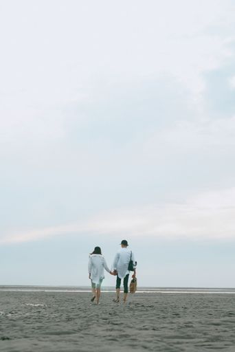 A joyful young couple walking along the beach, hand in hand - vertical love wallpaper