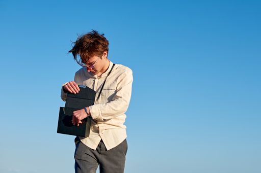A Caucasian man from Spain standing and opening his black handbag on clear sky background