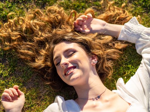 A young happy Spanish female with long hair spread out on the grass is resting in the spring park
