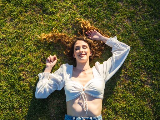 A top view of a happy Spanish female with long hair spread out on the grass is relaxing in the park