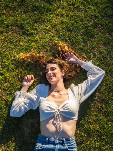 A top view of a young Spanish woman wearing a short white blouse is relaxing on the grass in the park