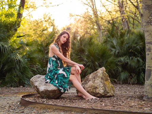 An elegant Spanish lady in the ornamented sundress sitting on the rock and posing in the spring park