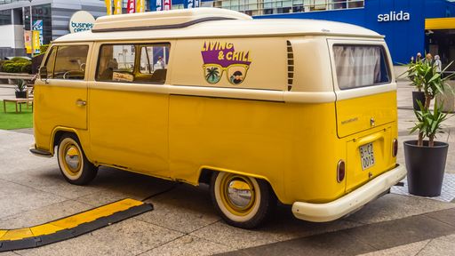 Yellow classic Volkswagen Van Camper Type 2. Vehicle parked in an esplanade of a shopping center.