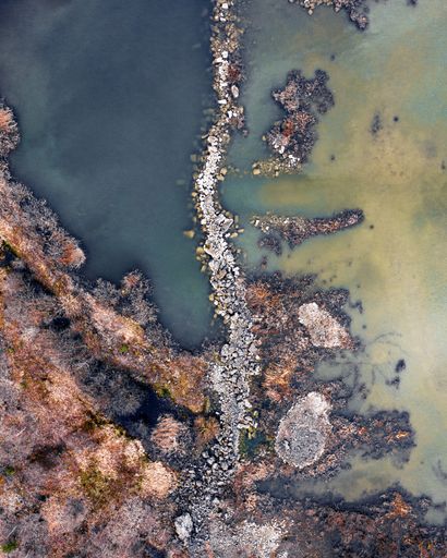 A vertical top down shot of a tidal creek separating two bodies of water - rocky path in the middle