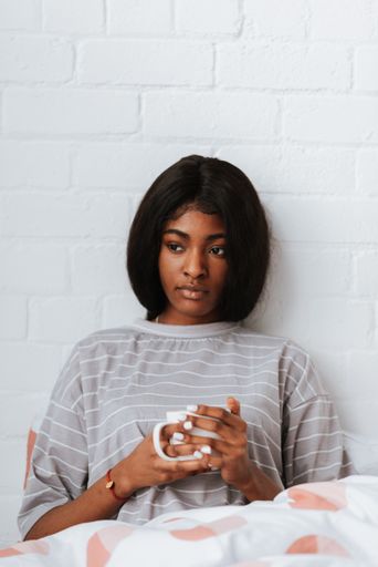 A beautiful young African female drinking a cup of coffee or tea while lying in bed after waking up in the morning