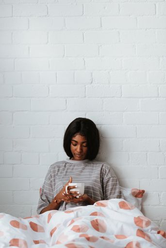 A beautiful young African female drinking a cup of coffee or tea while lying in bed after waking up in the morning
