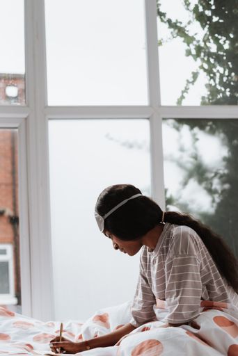 A pretty young African female with a sleeping eye mask on her head writing notes while sitting on bed