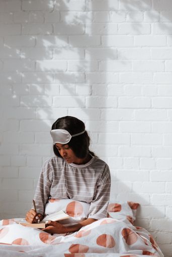 A lovely young African female with a sleeping eye mask on her head writing notes while sitting on bed