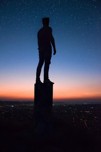 A silhouette of a man standing on a post, looking up at the night sky