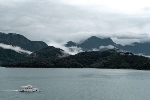 A small boat navigating in a lake covered with fog and mountain peaks in the background