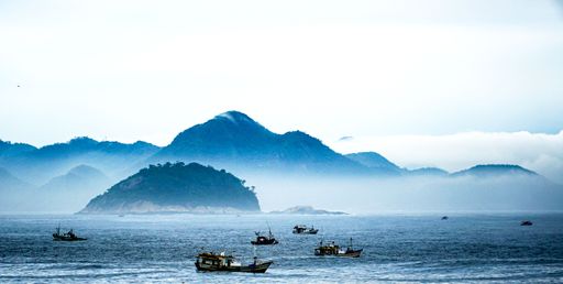 A scenic view of a fleet of boats sailing in the sea with a majestic mountain range in the background