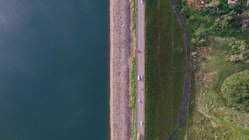 An aerial top view of a road near a lush park and blue water of Umiam Lake