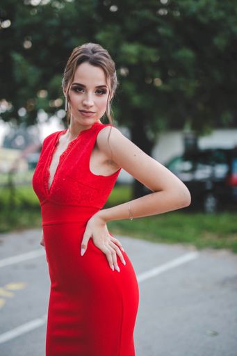 A sexy young Caucasian female in a red dress posing in a park