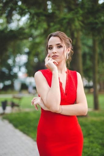 A sexy young Caucasian female in a red dress posing in a park