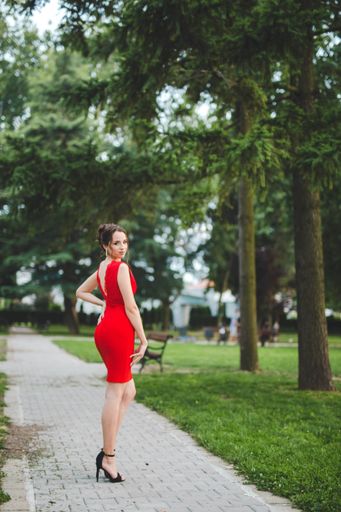A sexy and elegant Caucasian lady wearing a red dress and posing in the park