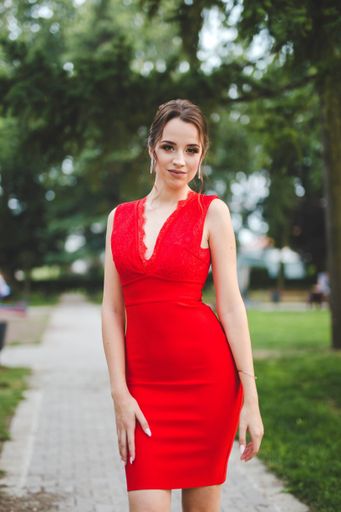 A pretty young Caucasian female wearing an elegant red dress posing in a park