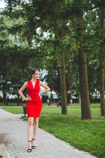 An attractive Caucasian female wearing an elegant red dress posing in a park