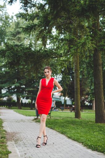 An attractive Caucasian female wearing an elegant red dress posing in a park