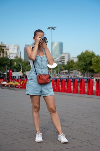 A vertical shot of a young blonde girl with a ponytail taking photos with her analog travel camera