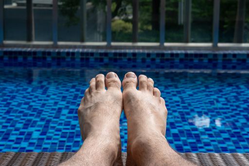 Close up of man's bare feet against swimming pool on a sunny day. Relaxing by the pool concept
