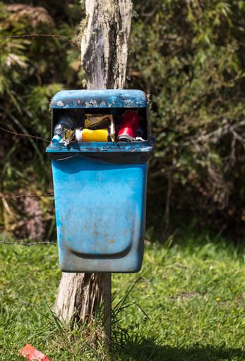 A vertical shot of a full trash can in a park