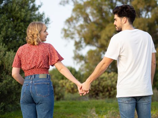 A back view of a cute young Spanish couple holding hands together and posing in the natural background