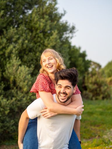 A young Spanish couple is having fun in the park; a guy is giving a piggyback ride to his girlfriend
