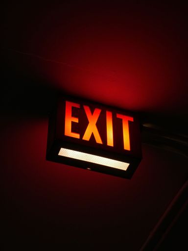 A well-lit exit sign illuminated in a dark setting against a wall