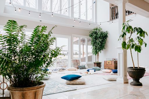 A closeup shot of a white room interior with carpets, pillows, lamps, and plants