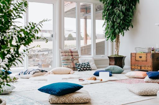 A closeup shot of a white room interior with carpets, pillows, lamps, and plants