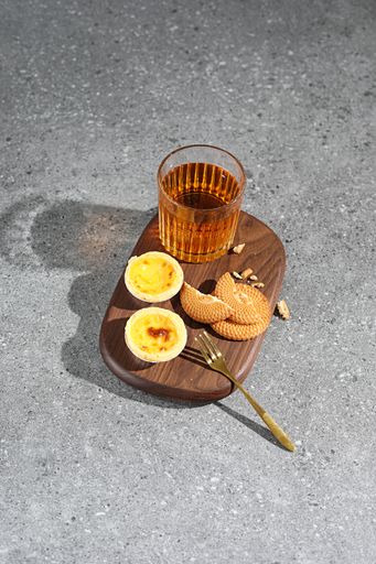 A wooden board with fresh pastries and a glass of tea on the concrete surface
