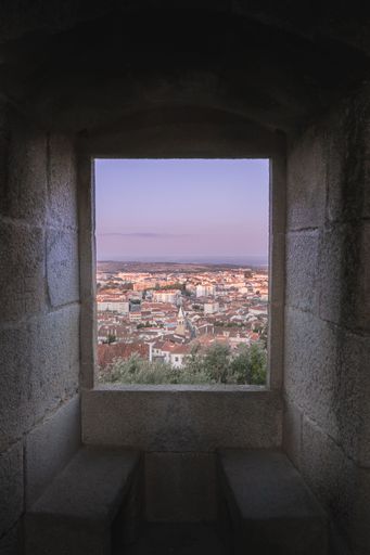 A vertical of sunset over an old town seen from a stone window