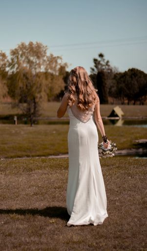 A vertical shot of a beautiful bride from the back holding the bouquet in a field