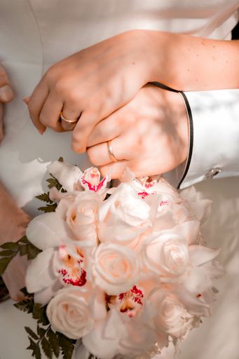 A vertical shot of the bride and groom's hands wearing rings, the bride holding the  bouquet