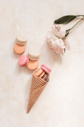 A top view of the sweet colorful macarons in the waffle cone on the light brown surface
