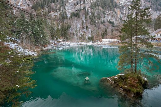 A stunning landscape of a tranquil turquoise lake surrounded by snow-capped mountains and evergreen forest