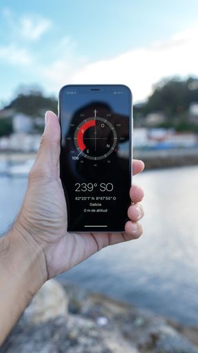 A hand holding a smartphone with a compass displayed on the screen on the background of the beach
