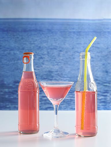 A glass of pink refreshing beverage sits in the foreground of a beach landscape, with several bottles in the background
