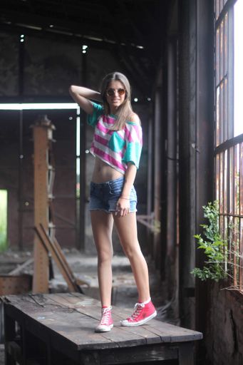 A vertical shot of a beautiful Caucasian lady wearing jeans shorts, crop top, sunglasses, sneakers