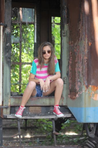 A vertical shot of a beautiful Caucasian lady wearing jeans shorts, crop top, sunglasses, sneaker