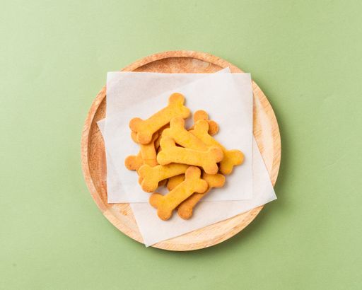 A selection of dog biscuits displayed on a wooden plate on a green surface