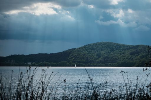 A beautiful landscape featuring a serene sea below dark, looming clouds, with lush hills in the background