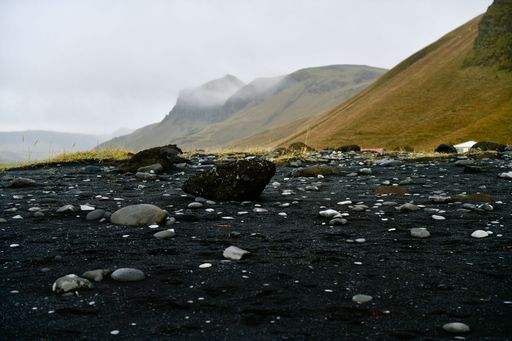 A rocky hillside, featuring large stones with green rolling hills with fog in the background