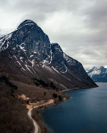 A snow-dusted mountain range, beside tranquil body of water, Eikesdalen, Norway