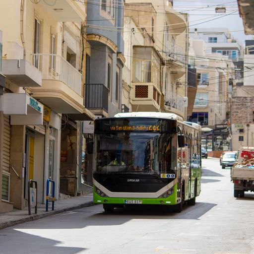 A vivid green public transport bus driving on a street between buildings.