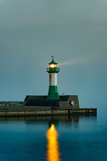 A vertical of a lighthouse on an illuminated pier reflecting in the sea on Rugen island, Germany