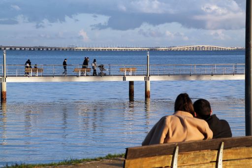 The two people sitting side by side on a wooden bench overlooking the beach with a dock