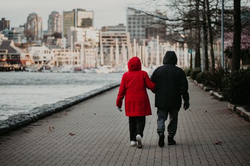 A rear view of a couple in coats walking on pavement bay walk