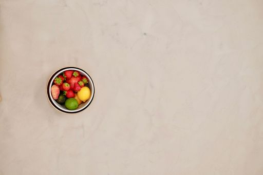 A top view of a small bowl with fresh colorful fruits on a white table
