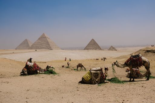 A group of camels and people take a break from their journey amongst the majestic pyramids in the Sahara desert